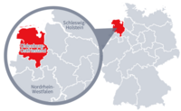 Diese Grafik zeigt eine Karte von Deutschland mit einer detaillierten Ansicht der Region Oldenburg-Ostfriesland. Oldenburg-Ostfriesland ist in Rot hervorgehoben und liegt im nördlichen Teil Deutschlands. Ein Lupensymbol vergrößert diesen Bereich, um die Lage genauer darzustellen.